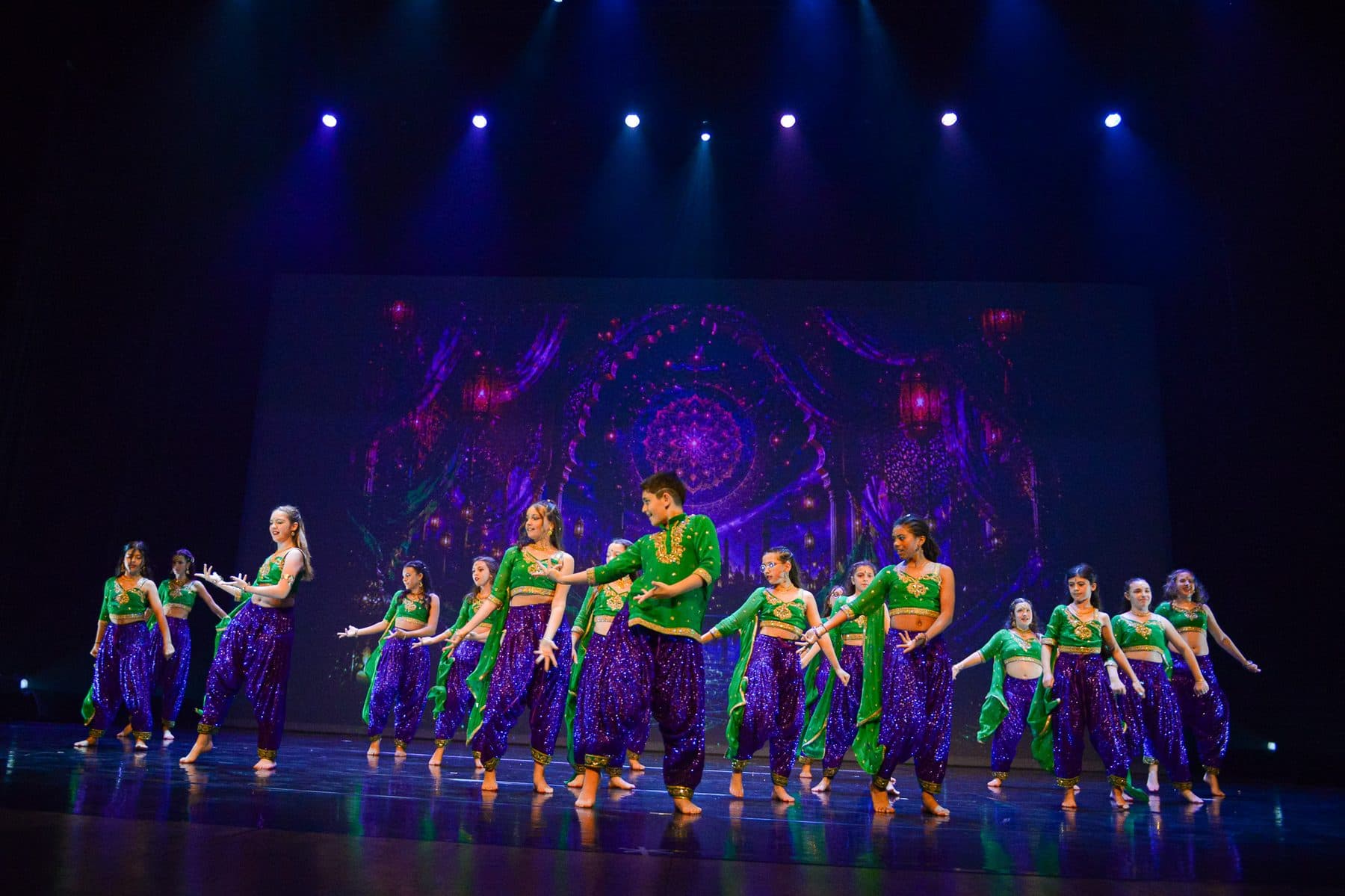 Groupe de danseuses en costumes violets et verts devant une projection lumineuse